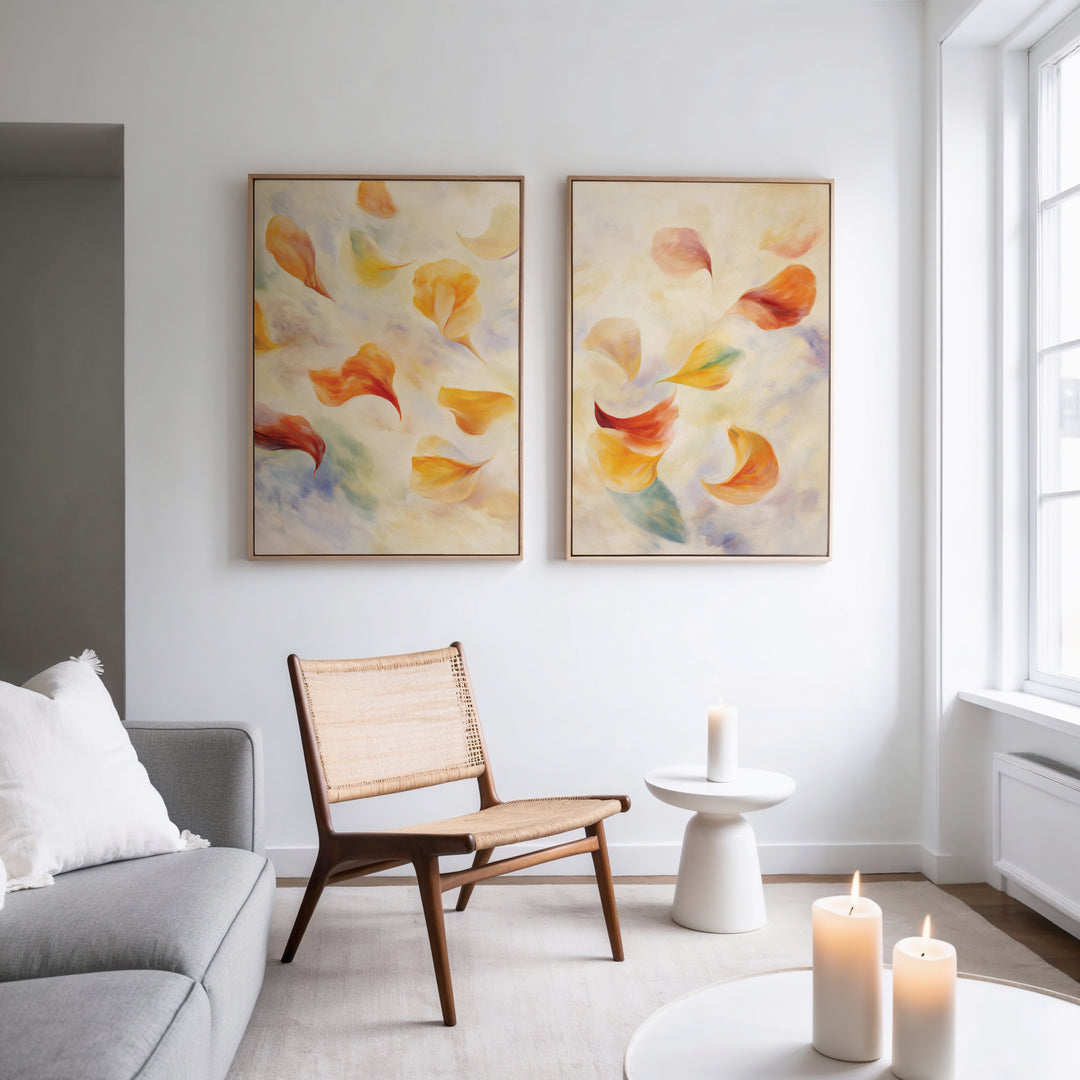 A modern living room features a light gray sofa, woven chair, and white side table with a candle. The “Floating Petals - Set of 2” canvas prints add color to the wall, while three candles glow on the round coffee table.