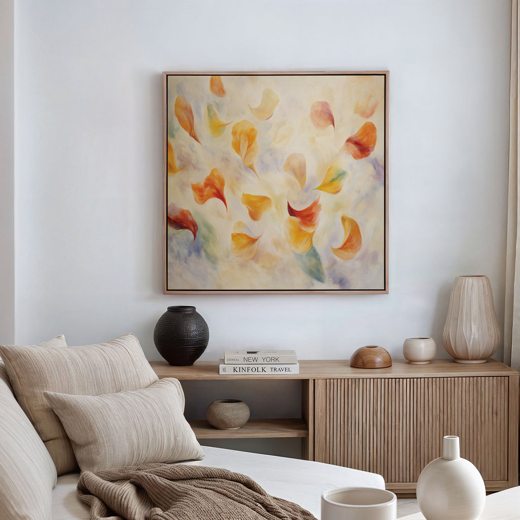 A cozy living room with a beige sofa, neutral decor, and a wooden sideboard features the Floating Petals Canvas Art - Square above it. Its abstract orange, yellow, and soft blue shapes add an elegant organic touch to the space.