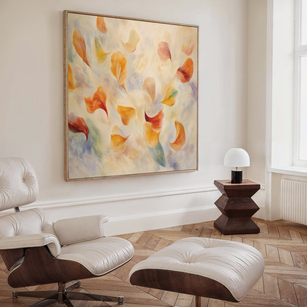 A modern living room with a white leather lounge chair, ottoman, wooden side table, small white lamp, and the Floating Petals Canvas Art - Square featuring swirling orange, yellow, and blue shapes that add organic elegance.