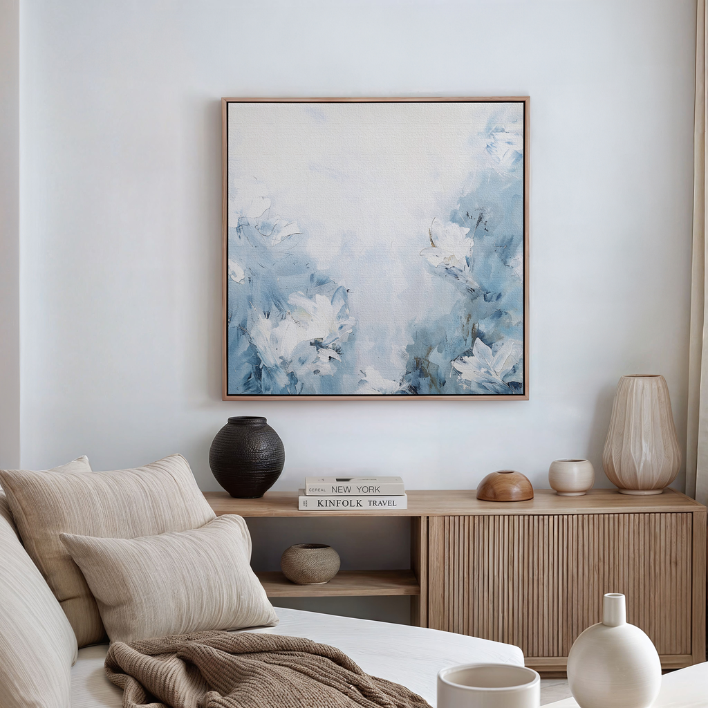 A modern living room corner with a beige sofa, neutral cushions, a wooden console table, decorative vases, stacked books, and the Spring Hues Abstract Canvas Art featuring blue and white florals hanging on a white wall.