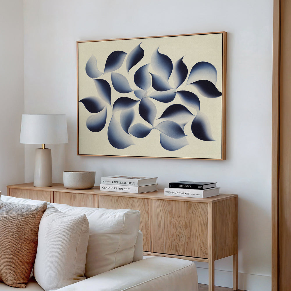 A modern living room with a light wood sideboard, books, a lamp, and ceramic bowls. Above the sideboard hangs the Flowing Shadows Canvas Art - Horizontal, displaying blue and gray organic shapes on a beige background.
