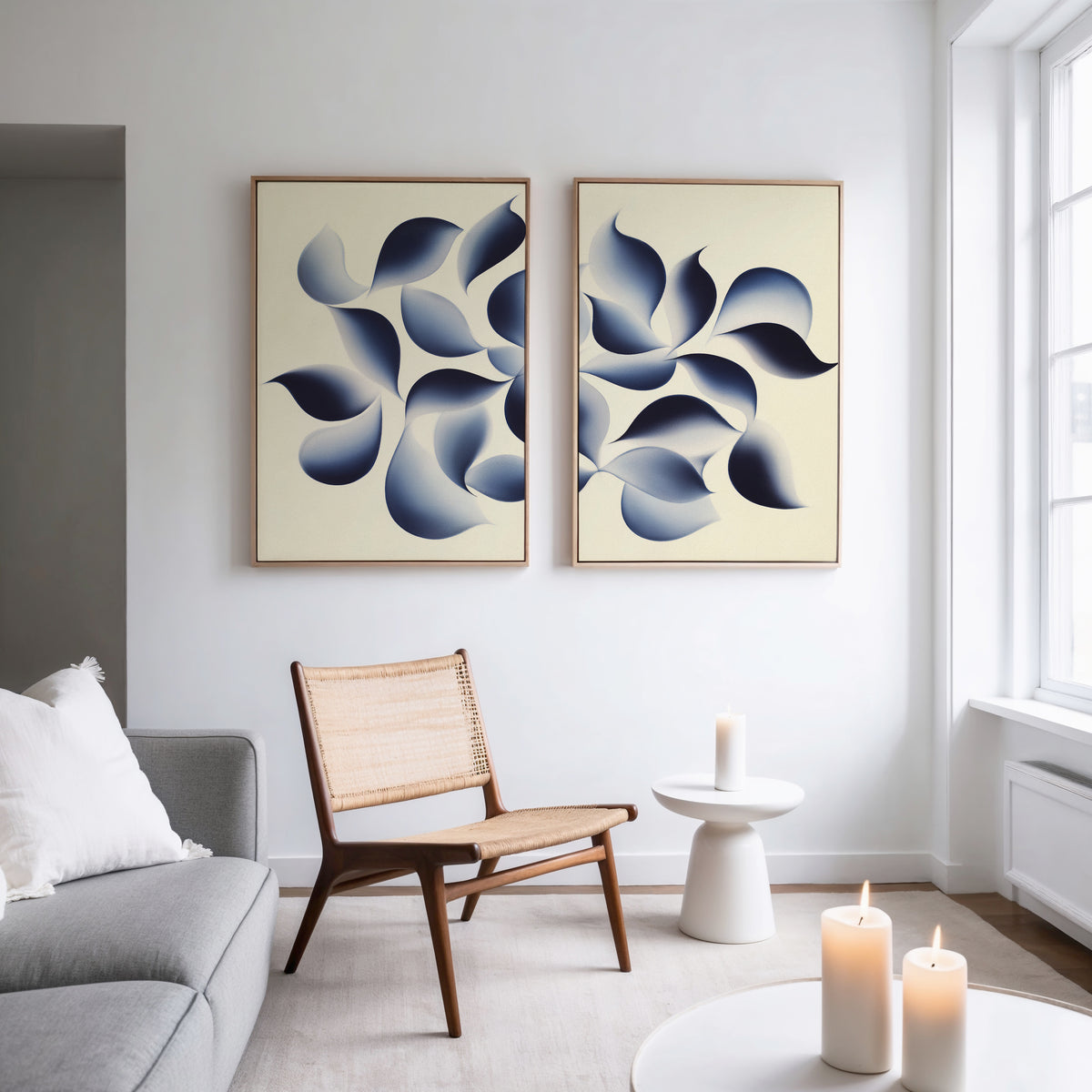 A modern living room with a gray sofa, wooden chair, and small round table. The Flowing Shadows - Set of 2 wall art adds style above, while large windows and candles create a bright, cozy atmosphere.
