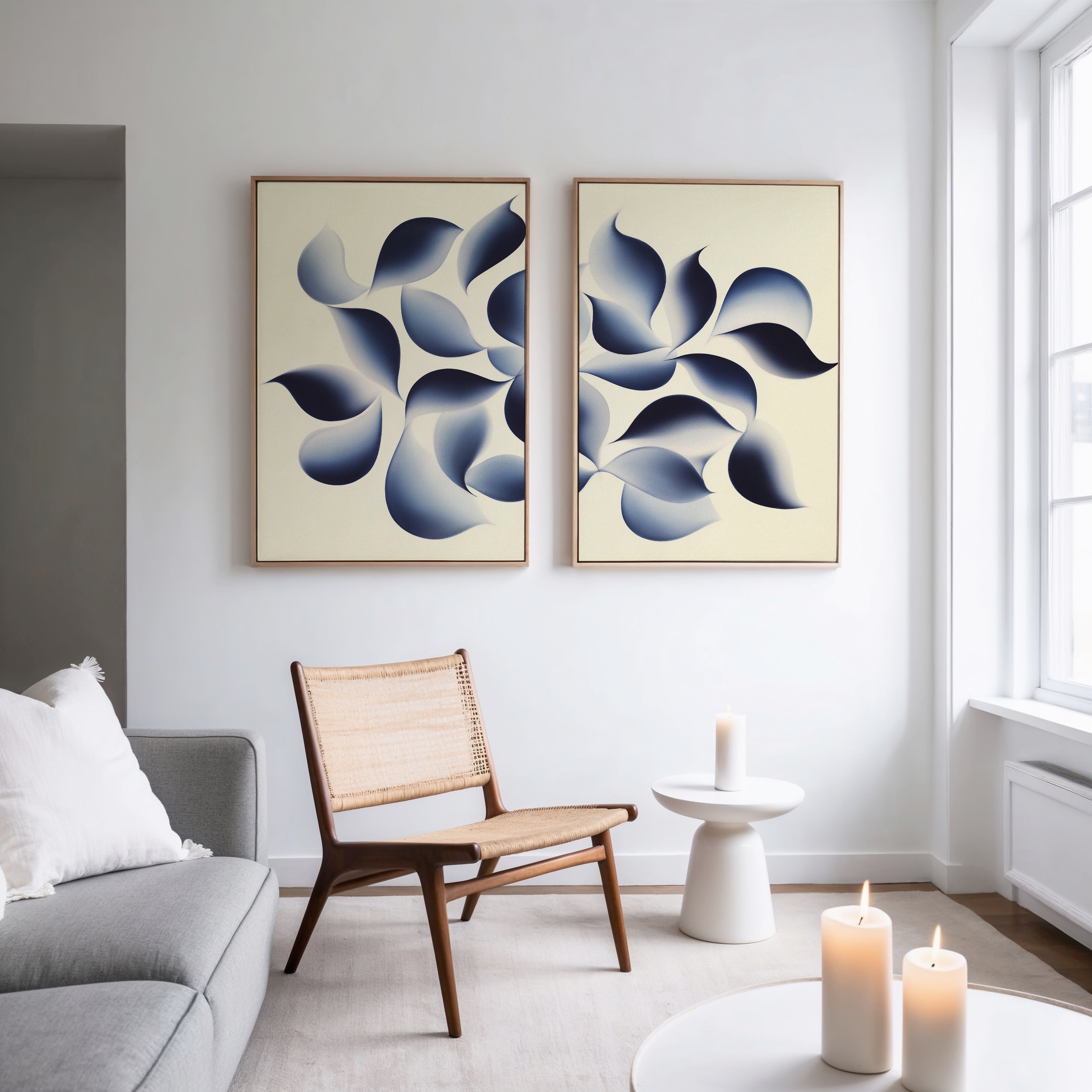 A modern living room with a gray sofa, wooden chair, and small round table. The Flowing Shadows - Set of 2 wall art adds style above, while large windows and candles create a bright, cozy atmosphere.