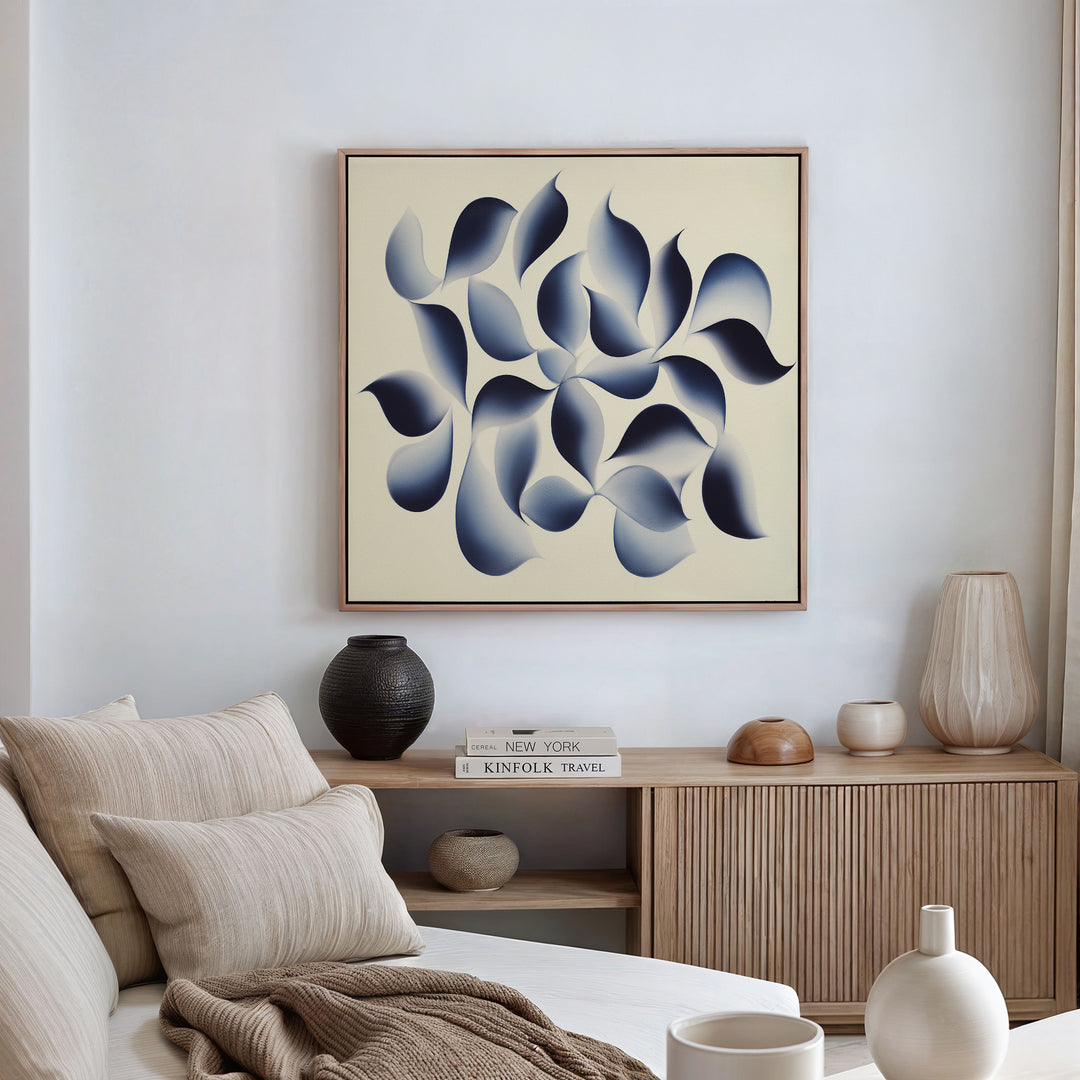 A modern living room features a beige sofa, neutral cushions, and a wooden sideboard topped with vases and books. Above hangs the Flowing Shadows Canvas Art - Square, adding an abstract indigo touch to the minimalist decor.