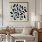 A modern living room with a neutral sofa, beige pillows, a wooden side table and lamp, and the Flowing Shadows Canvas Art – Square: an abstract indigo and gray print with curved shapes hanging above the couch.