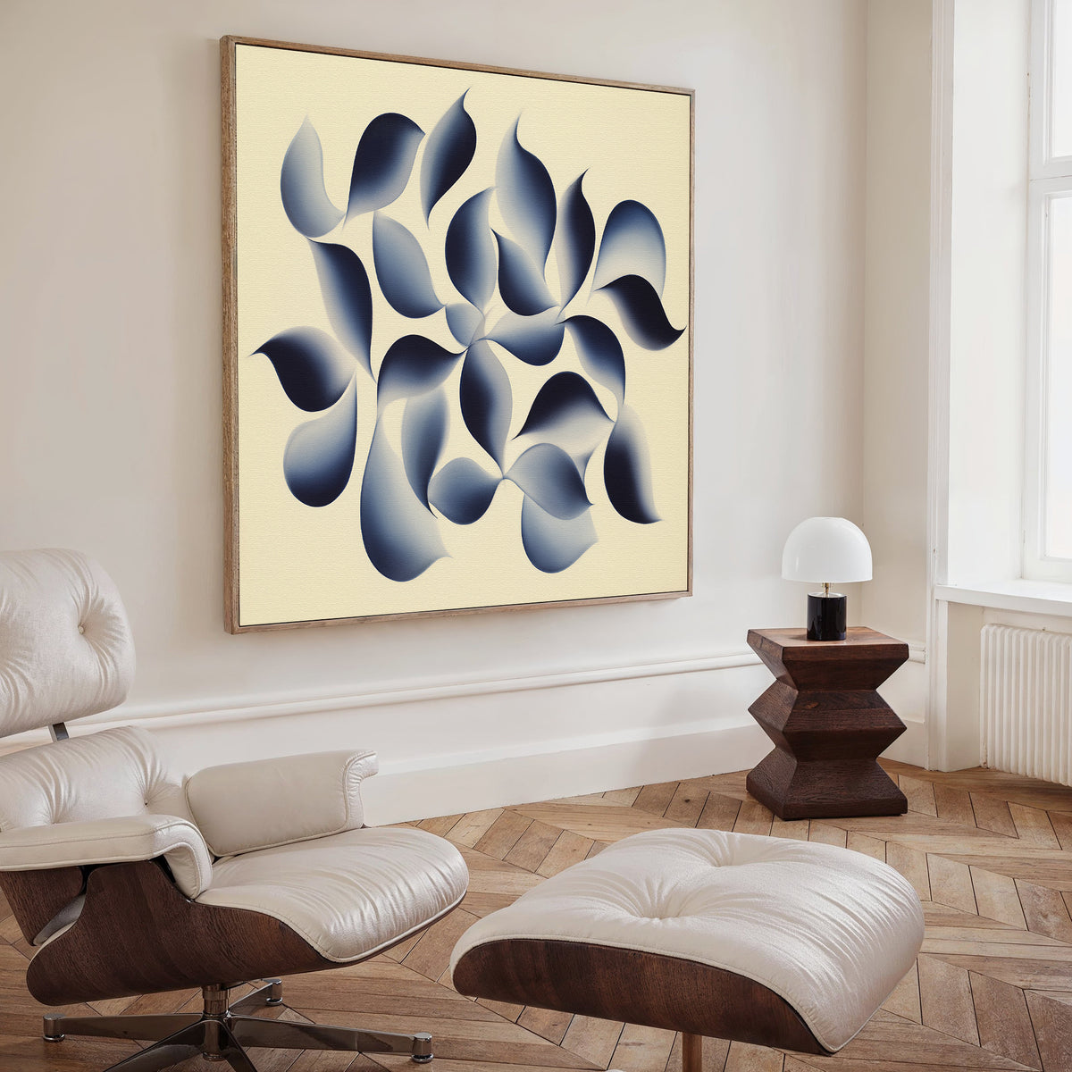 A modern living room with a light leather lounge chair and ottoman, wooden side table with a white lamp, and the Flowing Shadows Canvas Art - Square featuring blue and gray organic shapes on a cream background.