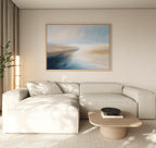 A modern living room with a light beige sectional sofa, low wooden coffee table with a dark bowl, tall plant, and the Fluid Motion Canvas Art - Horizontal in blue and beige tones creates a relaxing coastal atmosphere.