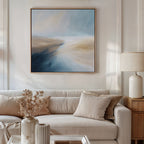 A modern living room with a beige sofa, neutral cushions, a wooden side table with a cream lamp, dried flowers in a vase, and the Fluid Motion Canvas Art - Square above the couch creates a relaxed coastal atmosphere.