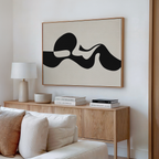 A modern living room features a light wood sideboard, white lamp, stacked books, and the Fluid Forms Abstract Canvas Art with bold black shapes in a neutral palette mounted above a white couch.