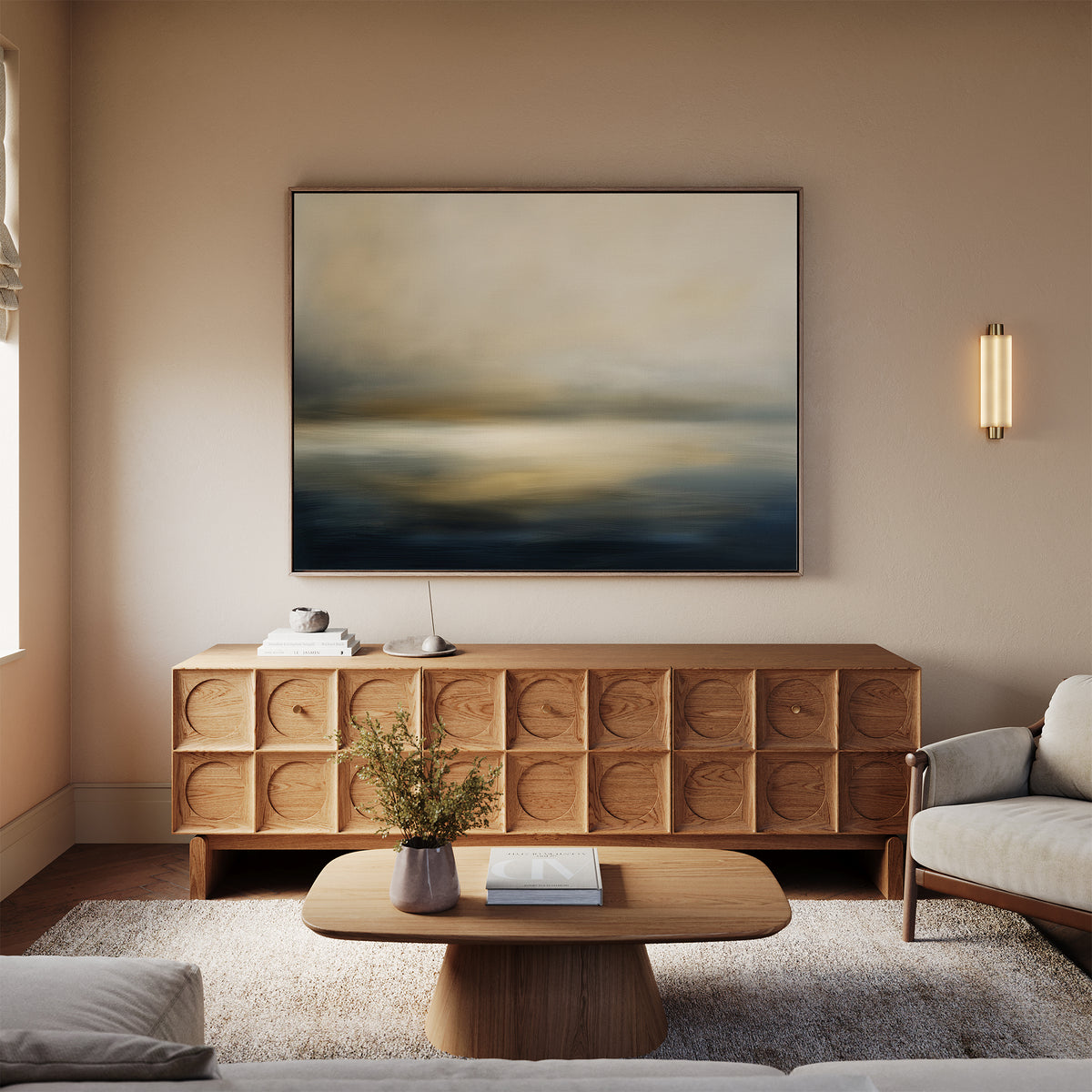 A modern living room with beige walls, the Foggy Bay Impressions Canvas Art - Horizontal above a wooden sideboard, a round coffee table with flowers, and cream sofas on a light rug creates serene Nordic Park-inspired décor.