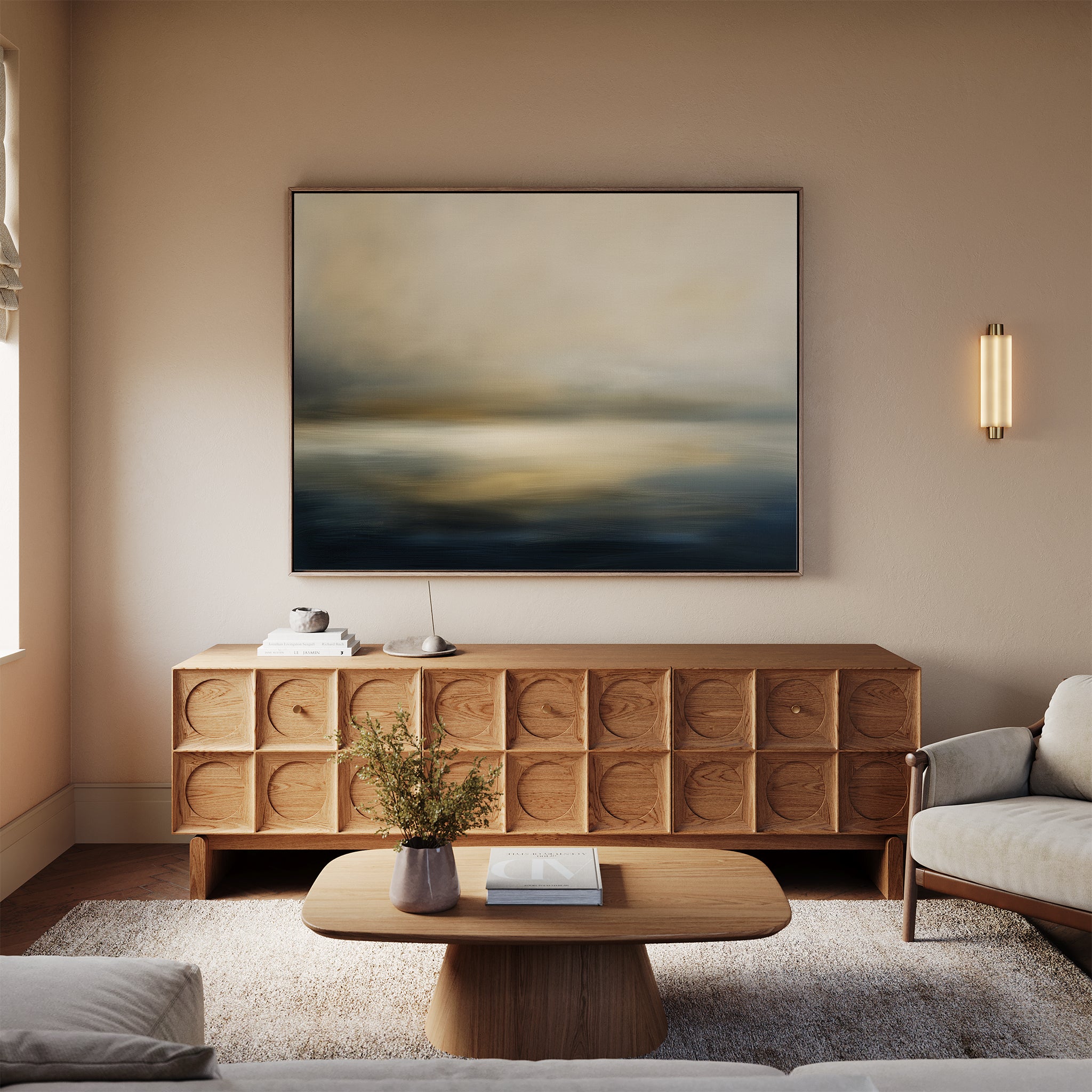 A modern living room with beige walls, the Foggy Bay Impressions Canvas Art - Horizontal above a wooden sideboard, a round coffee table with flowers, and cream sofas on a light rug creates serene Nordic Park-inspired décor.