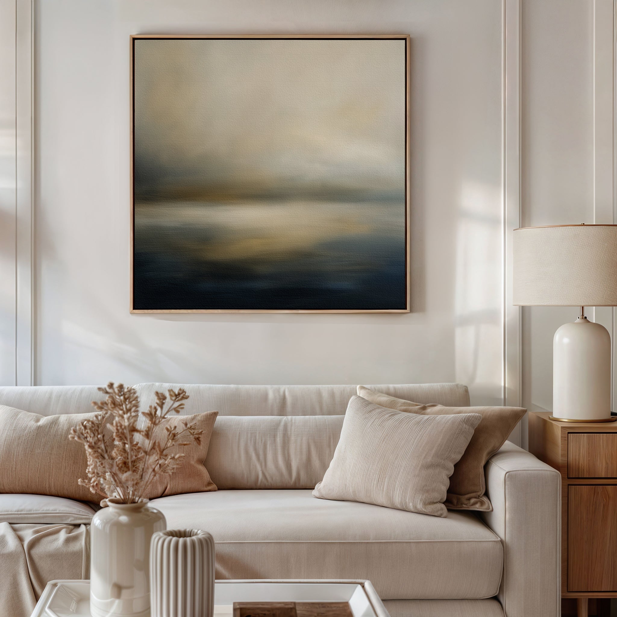 A modern living room with a beige sofa, neutral cushions, dried flowers in vases on a coffee table, a table lamp, and the Foggy Bay Impressions Canvas Art—square wall art with soft muted tones—brings Nordic Park tranquility to the space.