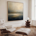 A modern living room featuring a white leather lounge chair with ottoman, a wooden side table with a small white lamp, and the Foggy Bay Impressions Canvas Art - Square brings Nordic Park-inspired tranquility to the space.