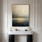 A modern, minimalist console table with decorative objects sits below the Foggy Bay Impressions Canvas Art – Vertical, its soft, blurred colors enhancing the serene elegance of the light-colored paneled wall.