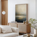 A modern living room with a light wood sideboard, Foggy Bay Impressions Canvas Art - Vertical, neutral vases, stacked books, a round pendant light, a white sofa with cushions, and a leafy plant in a beige pot exudes serene elegance.