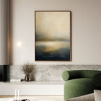 A modern living room featuring the Foggy Bay Impressions Canvas Art - Vertical in soft blue and beige, a green curved sofa, marble ledge, dried branches in a vase, and a wall light creates an air of serene elegance.