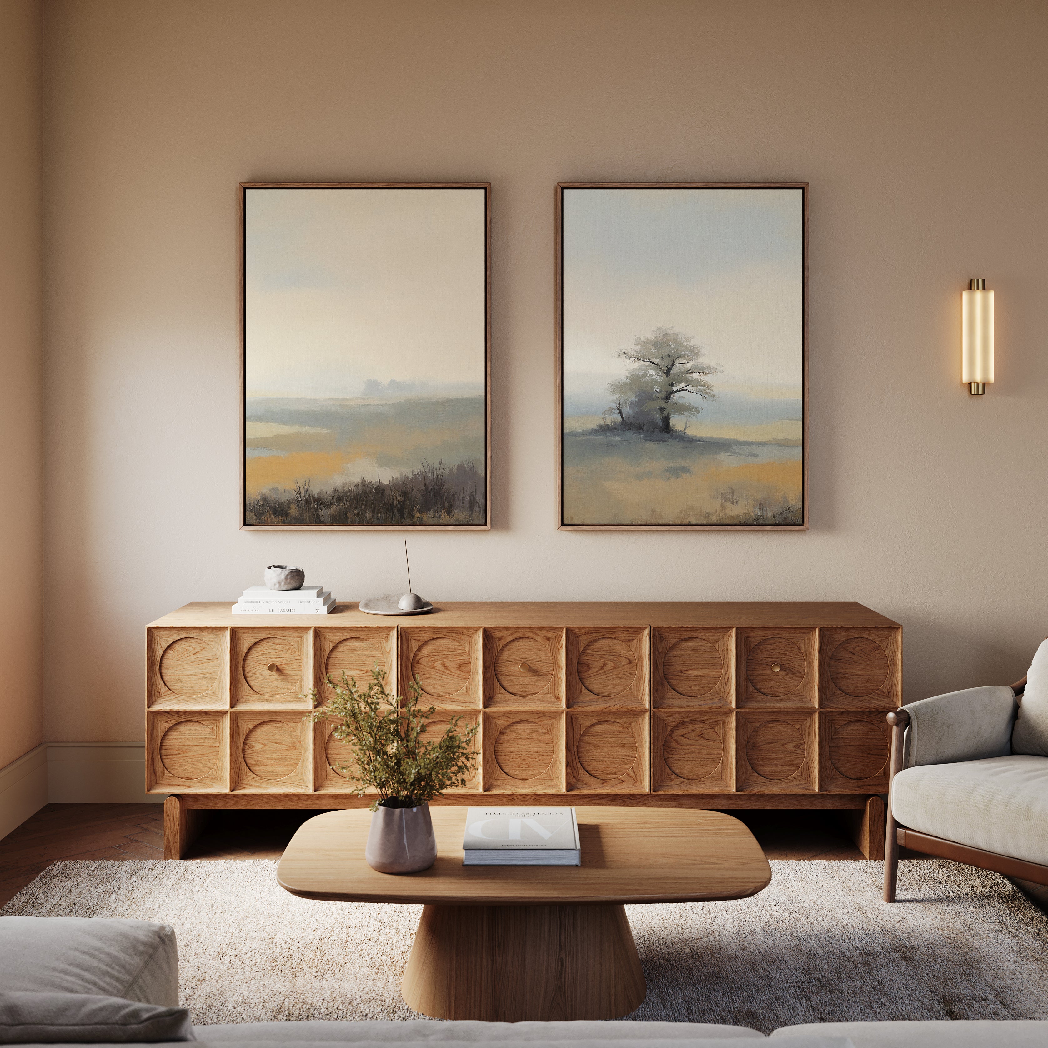 A modern living room with a wooden coffee table, matching sideboard, light sofa, and Foggy Solitude - Set of 2 misty landscape art above the sideboard. A small plant and books decorate the table and sideboard.