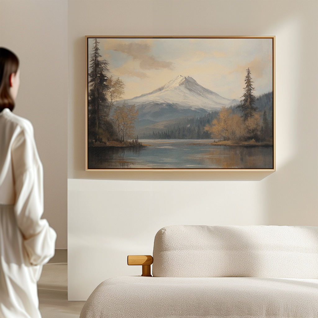 A person stands in a minimal, light-filled room, admiring the Frosted Ascent Canvas Art - Horizontal, which captures tranquil Nordic Park beauty and is displayed above a beige sofa.