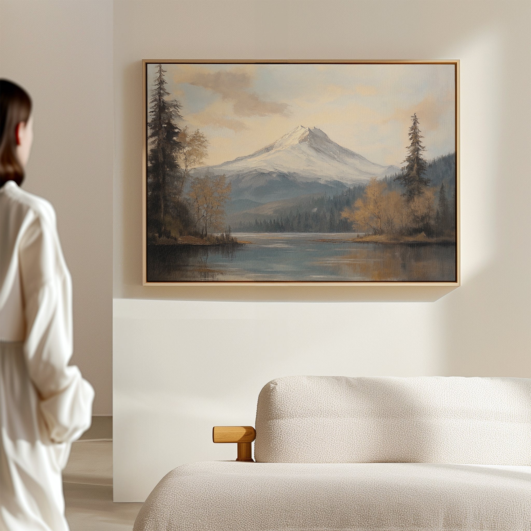 A person stands in a minimal, light-filled room, admiring the Frosted Ascent Canvas Art - Horizontal, which captures tranquil Nordic Park beauty and is displayed above a beige sofa.