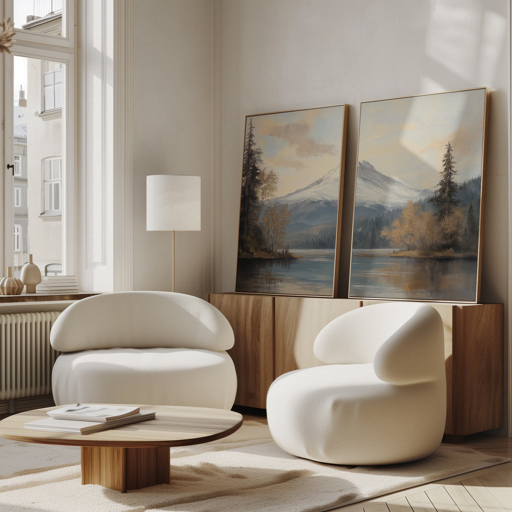 A modern living room features two rounded white chairs, a wooden coffee table, and a sideboard topped with the Frosted Ascent - Set of 2: tranquil mountain lake canvas art. Large windows fill the neutral space with natural light.