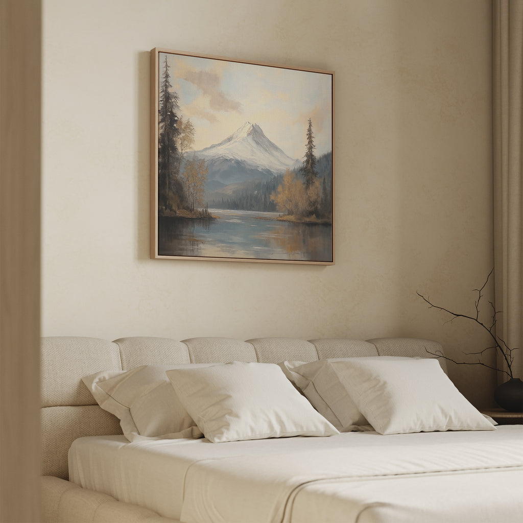 A beige bedroom with a low bed, white bedding, and four pillows features the Frosted Ascent Canvas Art - Square above the bed, showcasing serene mountains and water. A bare branch decorates the side table.