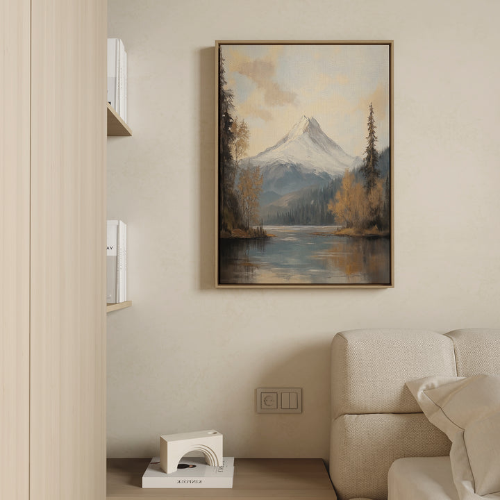 A cozy living room with a beige sofa, a low shelf with books and decor, and tranquil nature vibes—a "Frosted Ascent Canvas Art - Vertical" featuring mountains and a serene lake—hanging above the sofa.
