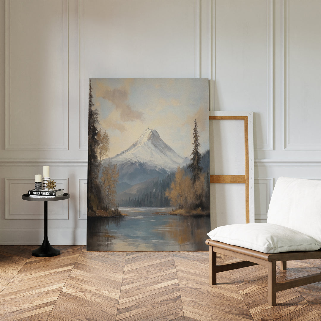 Frosted Ascent Canvas Art - Vertical, featuring a snow-capped mountain by a lake, rests against a white-paneled wall in a bright room with herringbone wood floors, a cushioned chair, candles on a small table, and an empty frame.