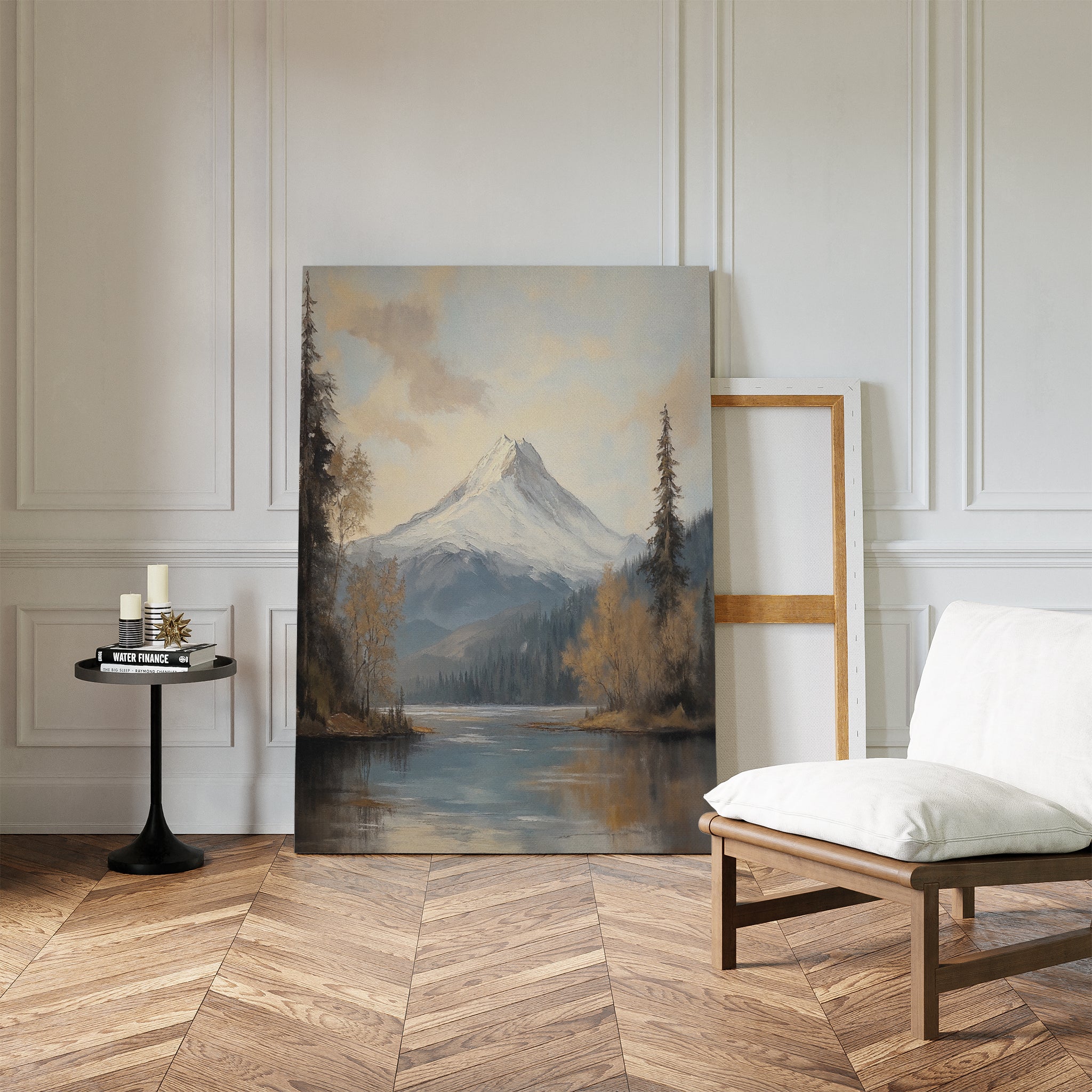 Frosted Ascent Canvas Art - Vertical, featuring a snow-capped mountain by a lake, rests against a white-paneled wall in a bright room with herringbone wood floors, a cushioned chair, candles on a small table, and an empty frame.