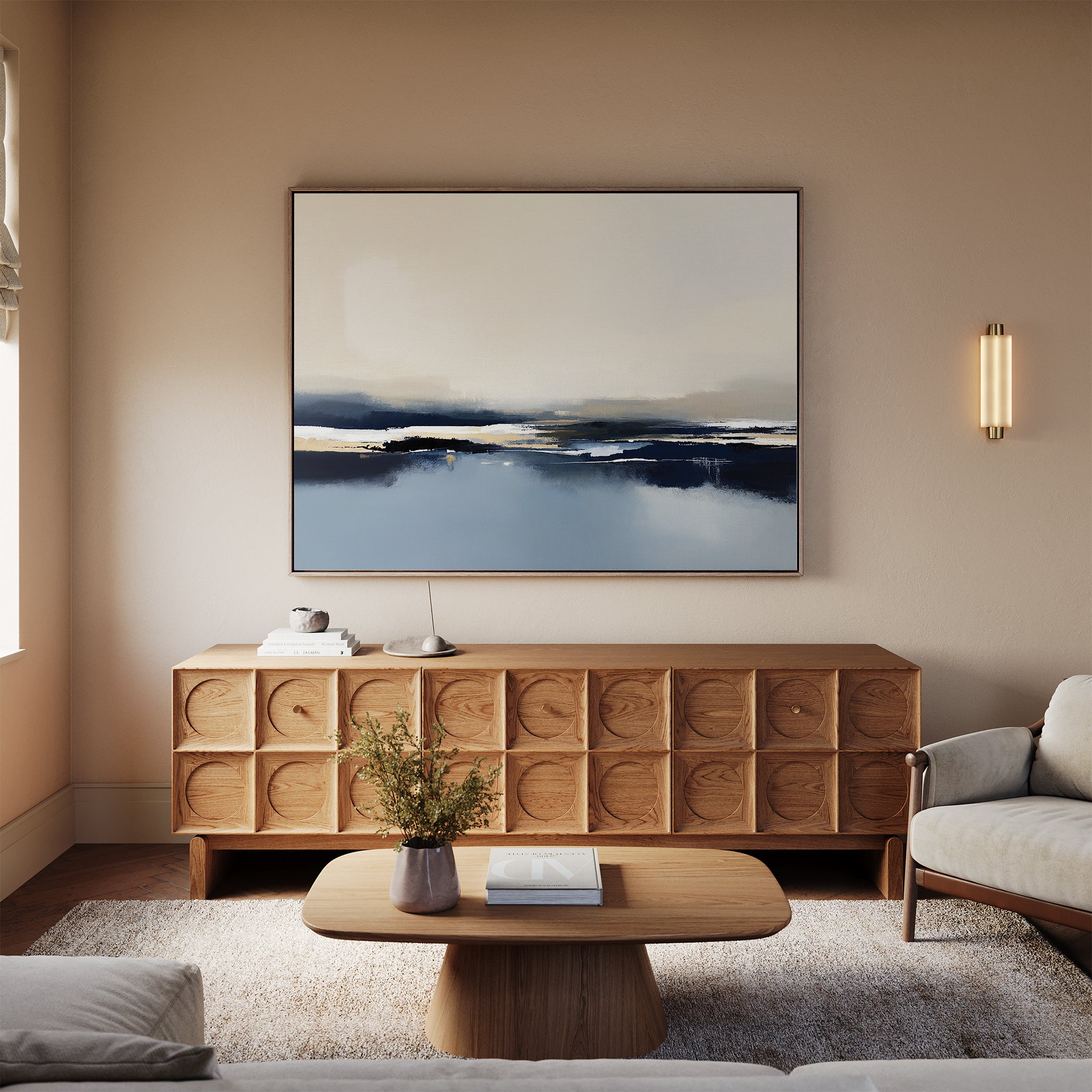 A modern living room features a wooden coffee table, textured sideboard, neutral-toned sofa, and the Frozen Bay Canvas Art - Horizontal, a large contemporary print in blue and white. A small vase with flowers sits on the table.