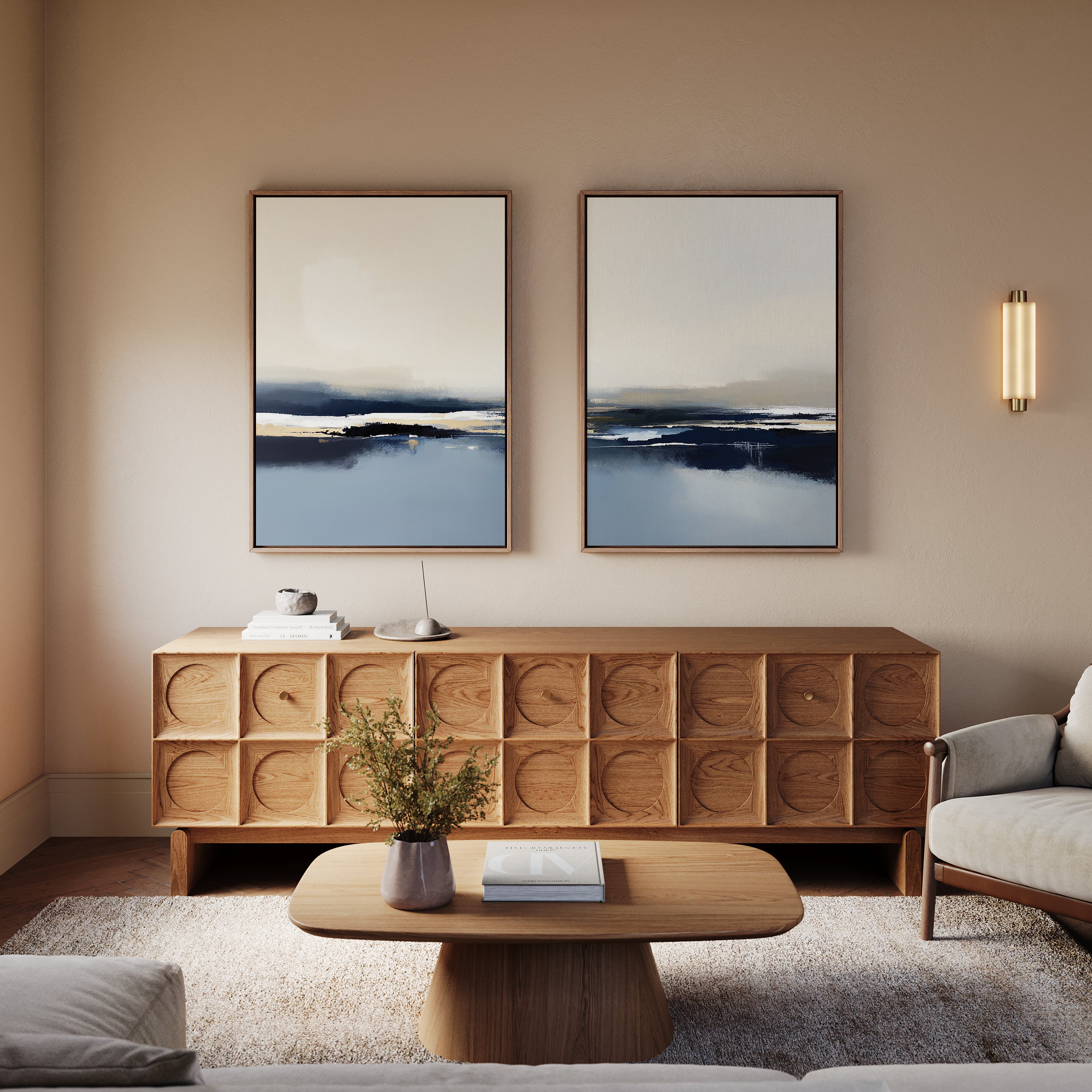 A modern living room features a wooden coffee table, matching sideboard, light sofa, and the Frozen Bay - Set Of 2 artworks above. A vase with greenery sits on the table; soft lighting enhances the cozy modern decor.