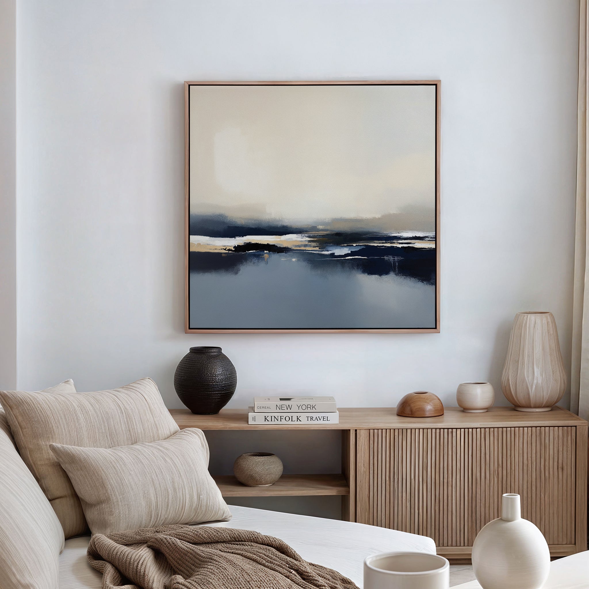 A minimal, modern living room with a beige sofa, neutral pillows, wooden sideboard, decorative vases, and the Frozen Bay Canvas Art - Square featuring abstract winter blues and beiges hanging on the wall.