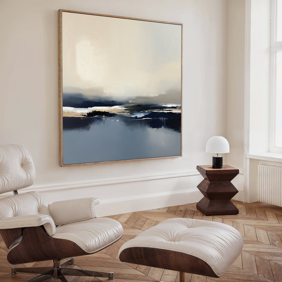 A modern living room showcases a white leather lounge chair with ottoman, a geometric wooden side table, and the Frozen Bay Canvas Art - Square in blue, white, and beige tones displayed on the wall.