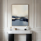 A minimalist room with white paneled walls, a marble console table displaying modern decor, and the Frozen Bay Canvas Art - Vertical—a contemporary blue, beige, and white print—hanging above.