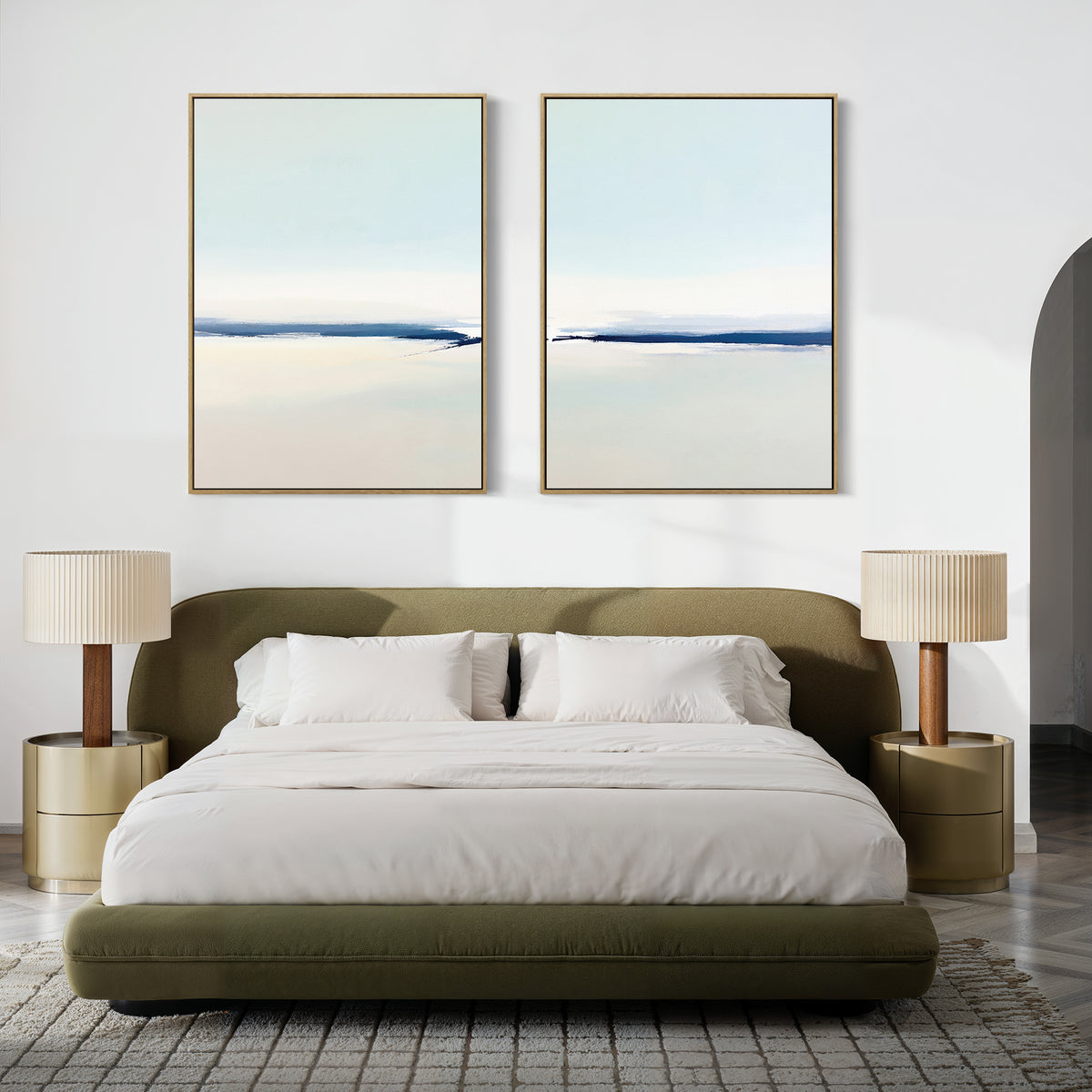A modern bedroom features a low olive-green bed with white bedding, two beige nightstands and matching lamps, and “Frozen Channel - Set Of 2” abstract landscape paintings above the bed on a crisp white wall.