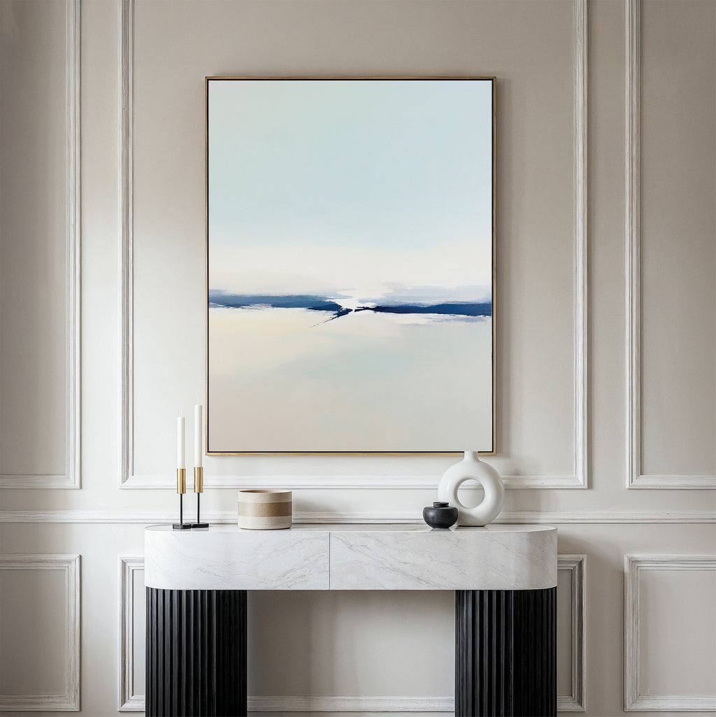 A minimalist room featuring the Frozen Channel Canvas Art - Vertical in soft blue, white, and beige tones on a beige paneled wall with a marble console table and decorative objects—ideal for modern living room decor.