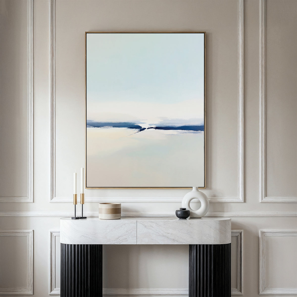 A minimalist room featuring the Frozen Channel Canvas Art - Vertical in soft blue, white, and beige tones on a beige paneled wall with a marble console table and decorative objects—ideal for modern living room decor.