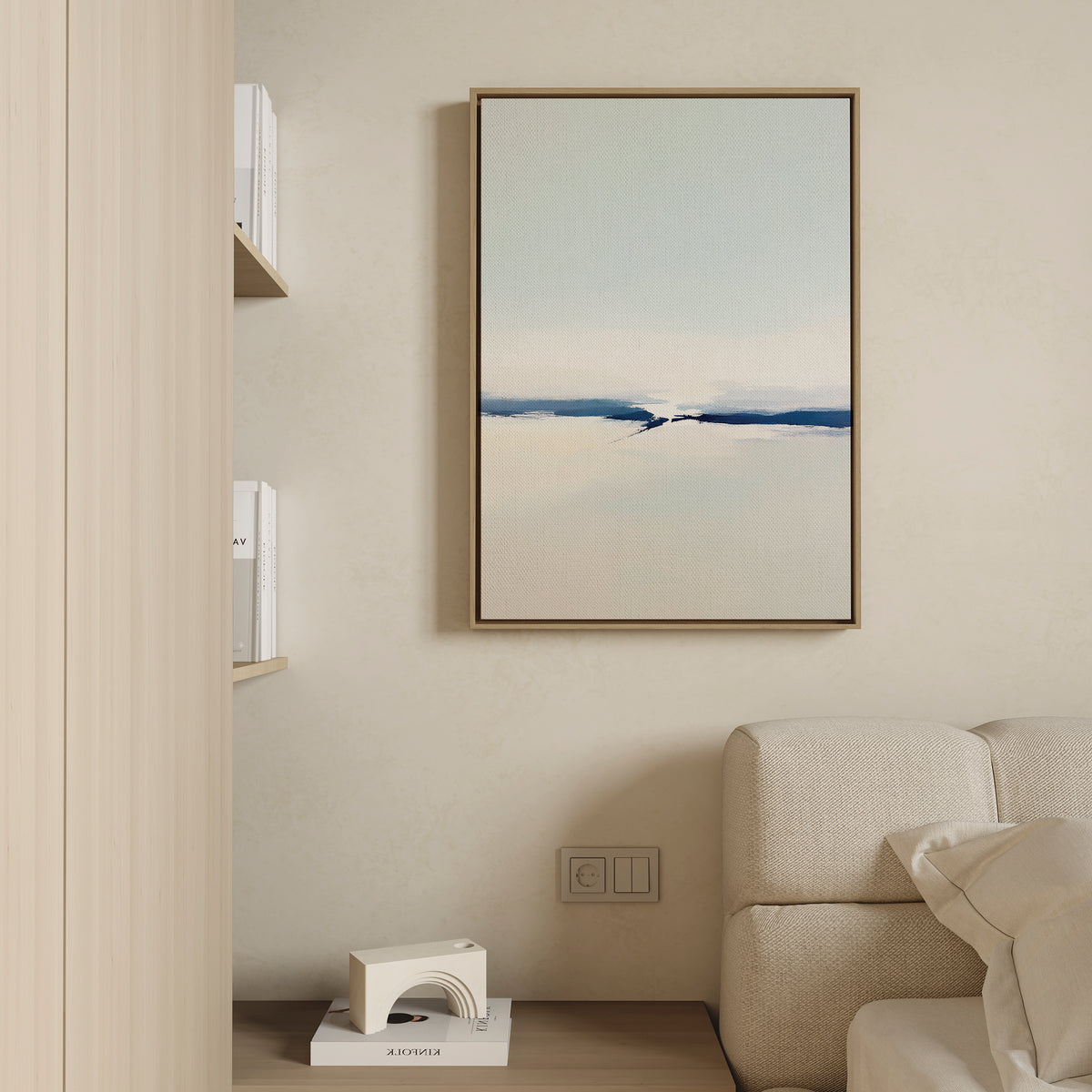 A minimalist living room corner features a beige sofa, built-in bookshelves, and the Frozen Channel Canvas Art - Vertical in calming blue tones as modern wall decor above an electrical outlet.