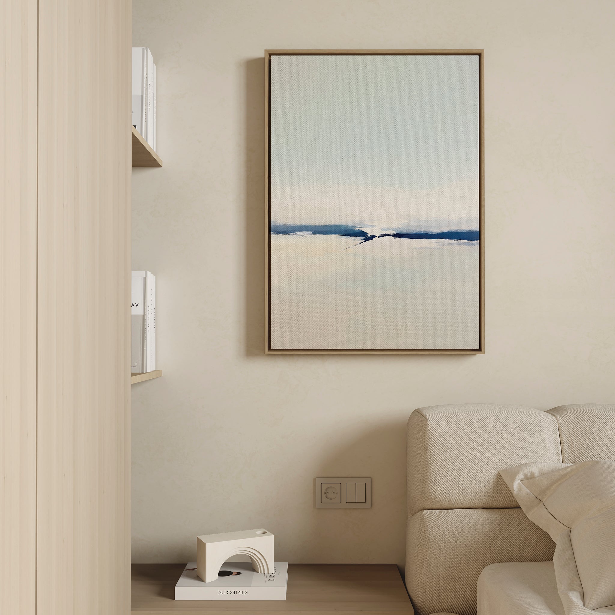 A minimalist living room corner features a beige sofa, built-in bookshelves, and the Frozen Channel Canvas Art - Vertical in calming blue tones as modern wall decor above an electrical outlet.