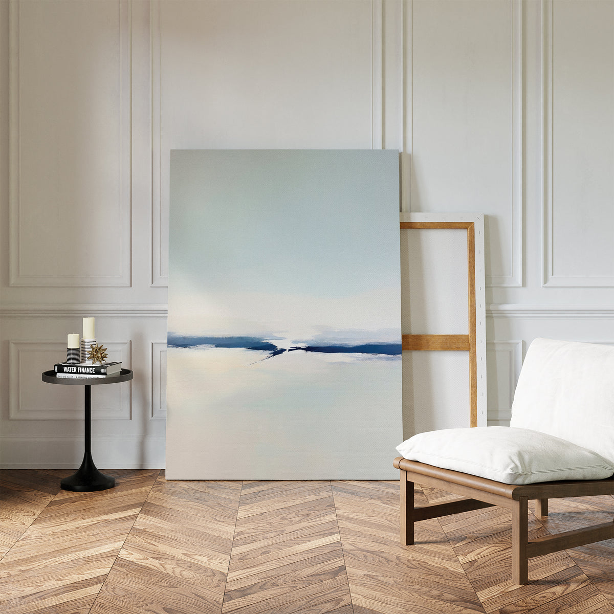 A minimalist room with herringbone wood floors, white paneled walls, modern decor, a cushioned chair, a small black table with candles and books, and the Frozen Channel Canvas Art - Vertical leaning against the wall.