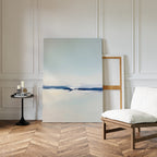 A minimalist room with herringbone wood floors, white paneled walls, modern decor, a cushioned chair, a small black table with candles and books, and the Frozen Channel Canvas Art - Vertical leaning against the wall.