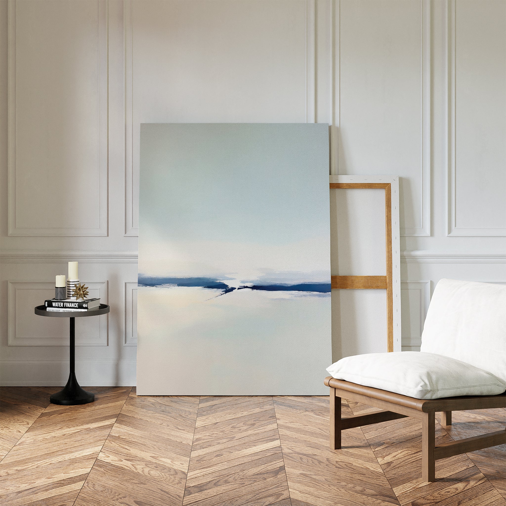 A minimalist room with herringbone wood floors, white paneled walls, modern decor, a cushioned chair, a small black table with candles and books, and the Frozen Channel Canvas Art - Vertical leaning against the wall.