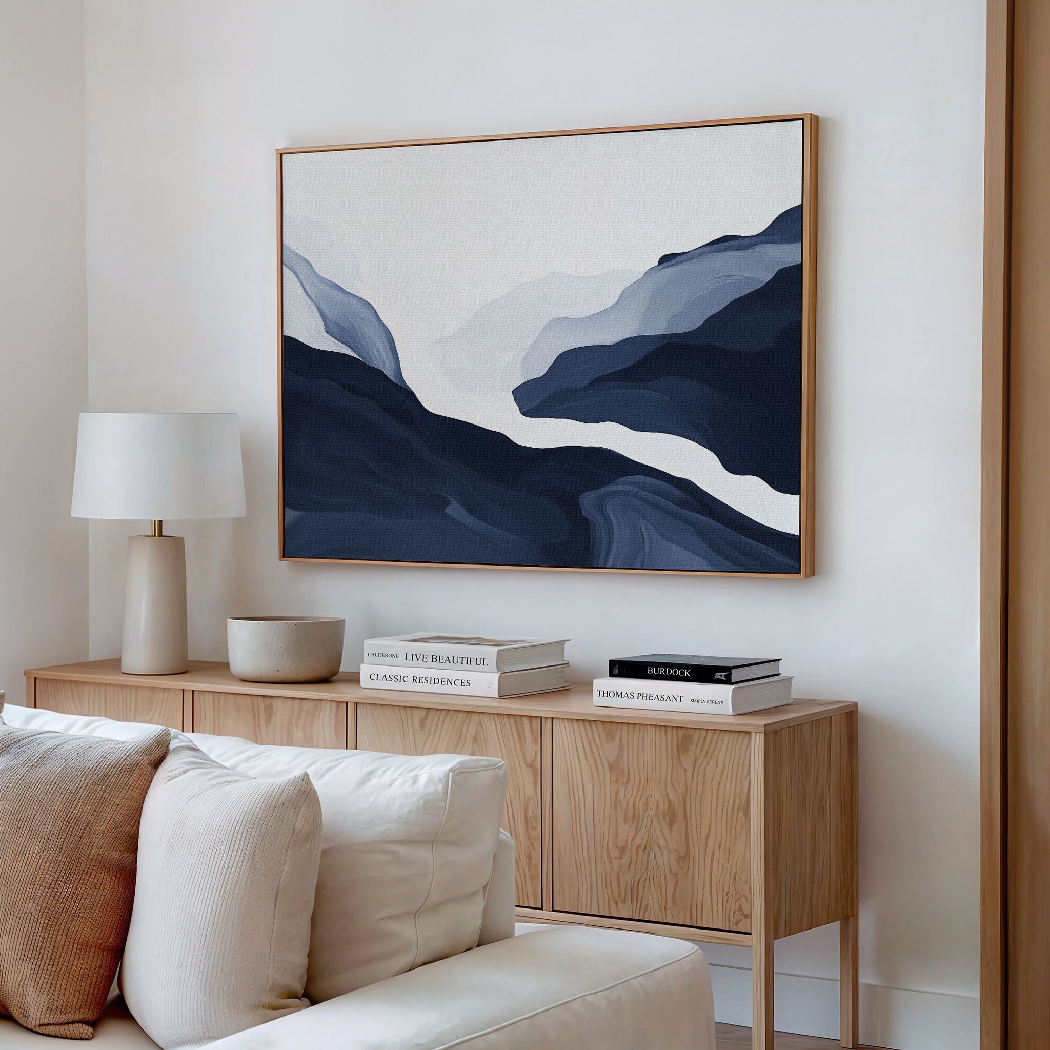 A modern living room featuring the Glacier Flow Canvas Art - Horizontal, a wooden sideboard, white table lamp, books, bowl, and a white sofa with cushions. The minimalist decor uses neutral tones for a contemporary feel.