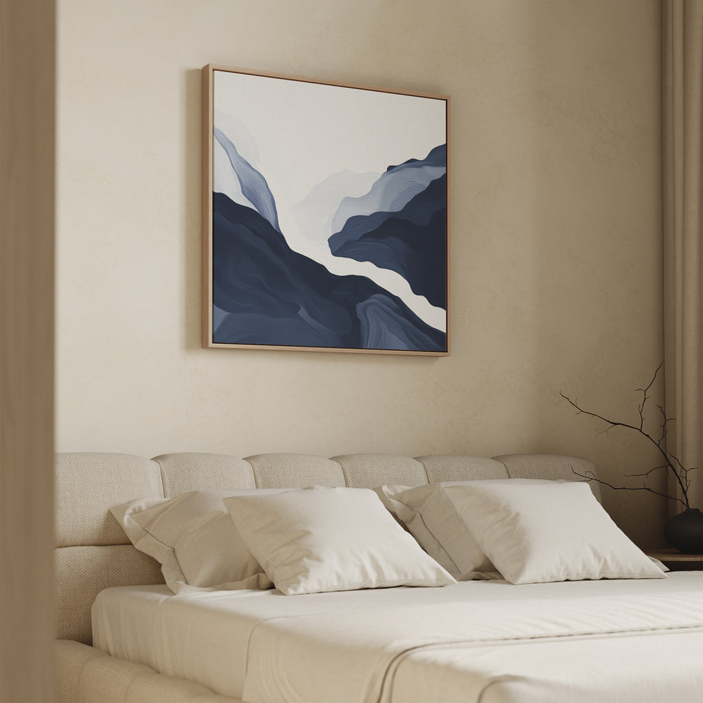 A modern bedroom features a beige upholstered bed with cream bedding and pillows. Above the bed hangs the Glacier Flow Canvas Art - Square, while light enters through a window with neutral curtains.