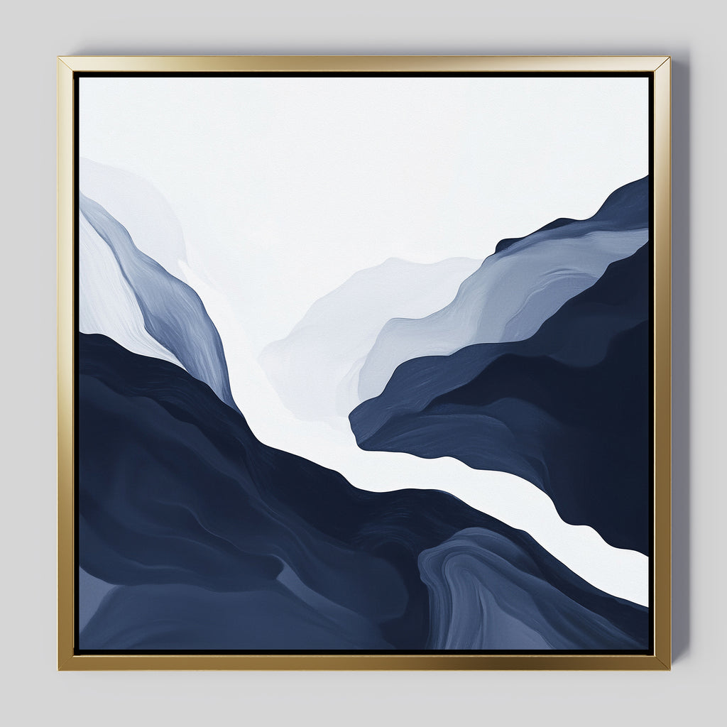 The Glacier Flow Canvas Art - Square features flowing wavy shapes in deep blue, gray, and white, resembling mountains or valleys. This modern piece is framed in a thin gold frame and displayed on a light gray wall.