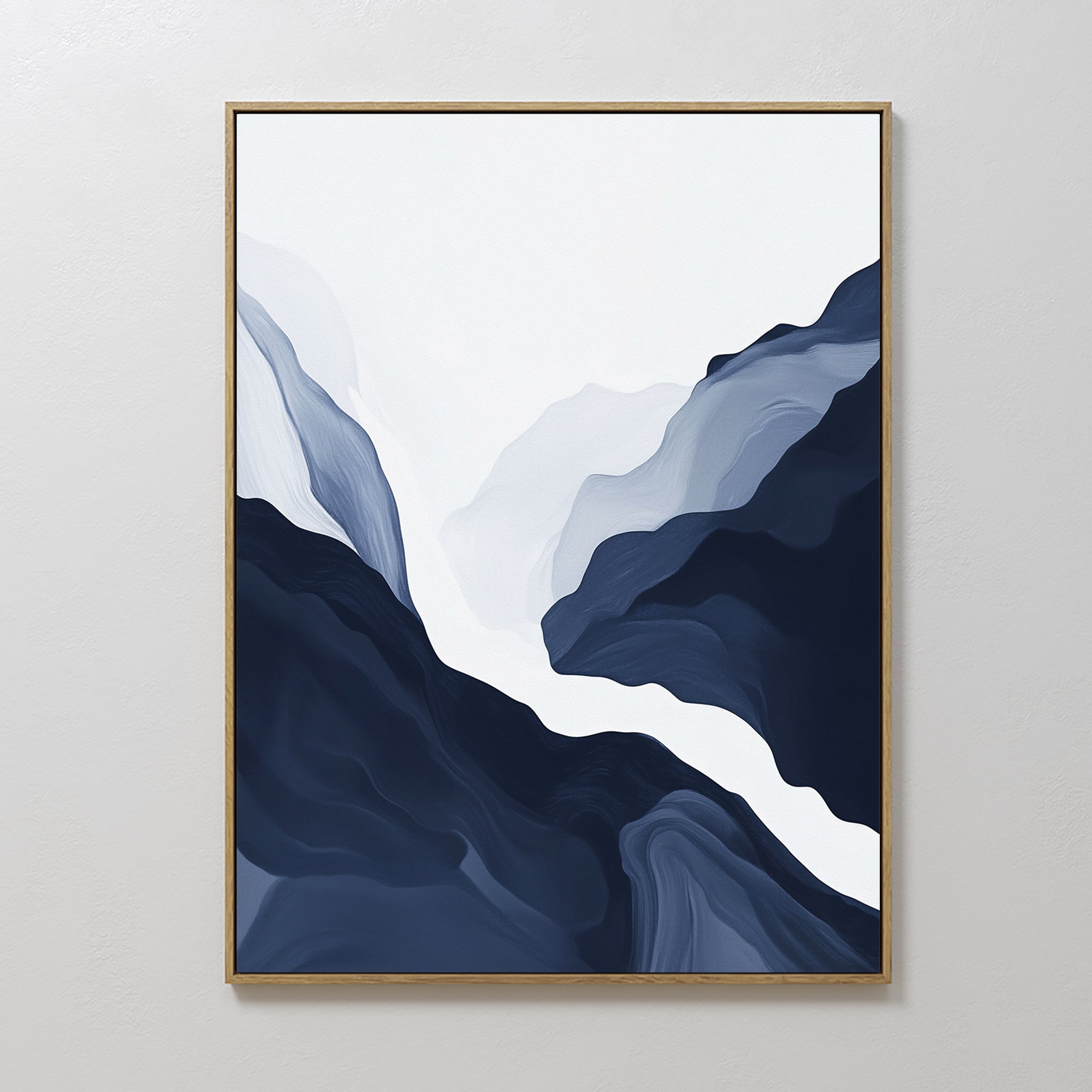 Glacier Flow Canvas Art - Vertical features flowing, layered shapes in deep blue, gray, and white that evoke a mountain or river landscape. Framed in thin gold, this modern decor piece hangs elegantly on a white wall.