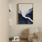 Minimalist living room featuring a light beige sofa, wooden bookshelf of books, and Glacier Flow Canvas Art - Vertical in a wooden frame on a cream wall. A geometric floor decor piece enhances the modern home aesthetic.