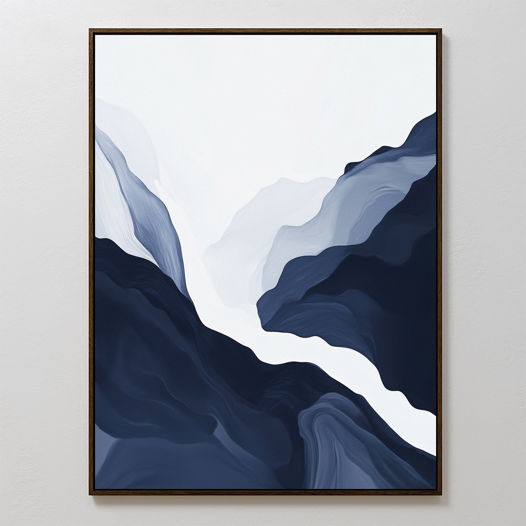 The Glacier Flow Canvas Art - Vertical features abstract flowing shapes in navy blue, gray, and white, evoking a mountain landscape with a river. This modern piece is framed with a thin dark border and displayed on a white wall.