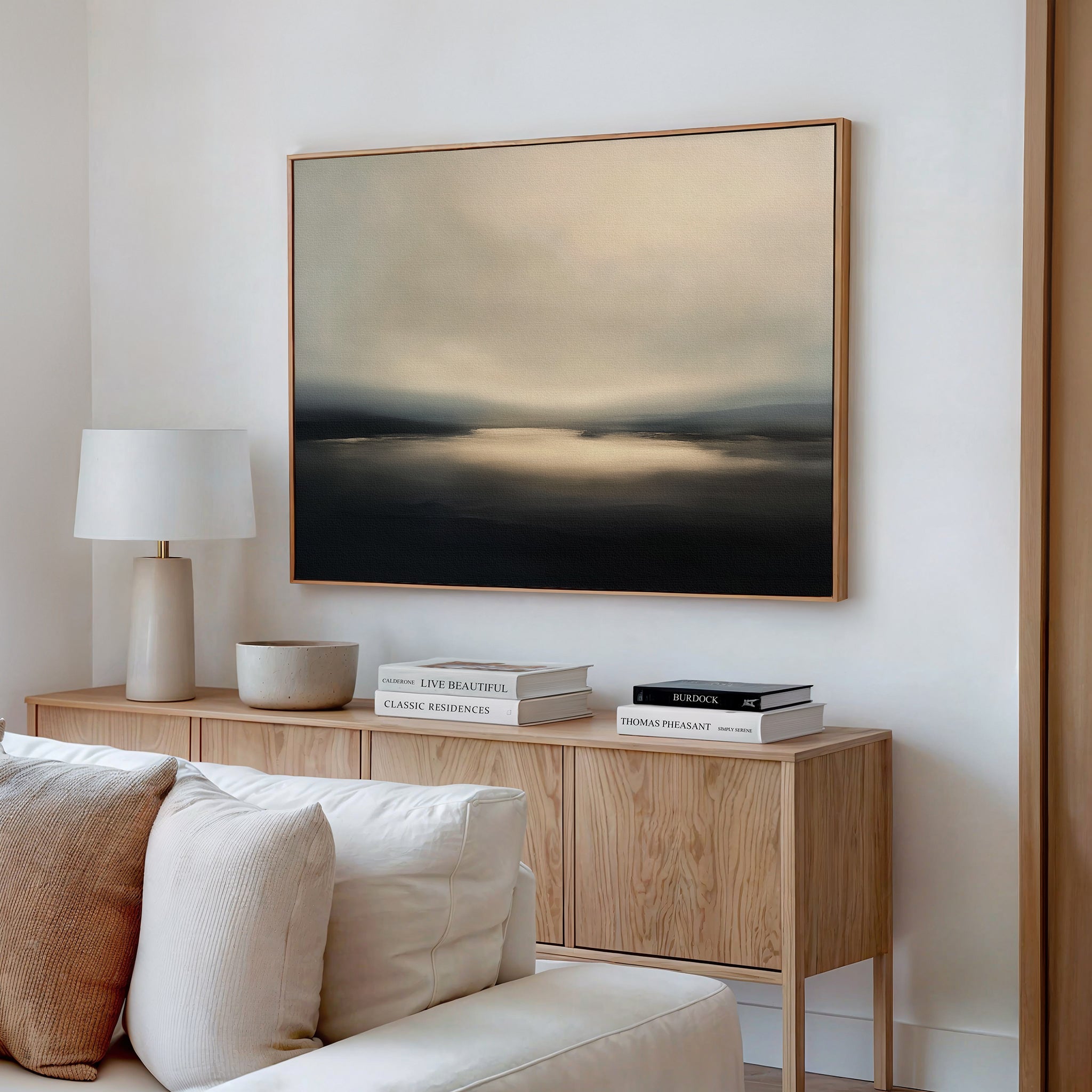 A minimalist living room features a wooden sideboard topped with a table lamp, stacked books, and a bowl. Above hangs the Golden Fog Horizon Canvas Art—a large abstract landscape in soft beige and gray—creating a serene atmosphere.