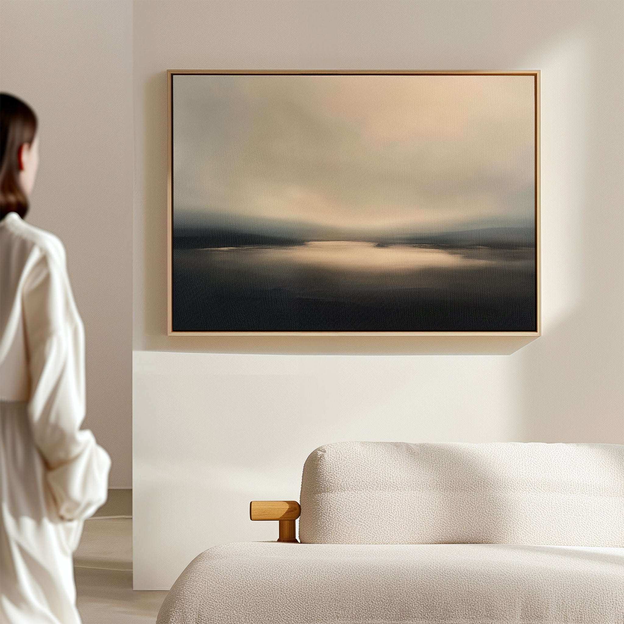 A person stands in a softly lit room, facing the Golden Fog Horizon Canvas Art - Horizontal above a light-colored textured sofa; the wall art’s muted tones evoke serenity and calm.