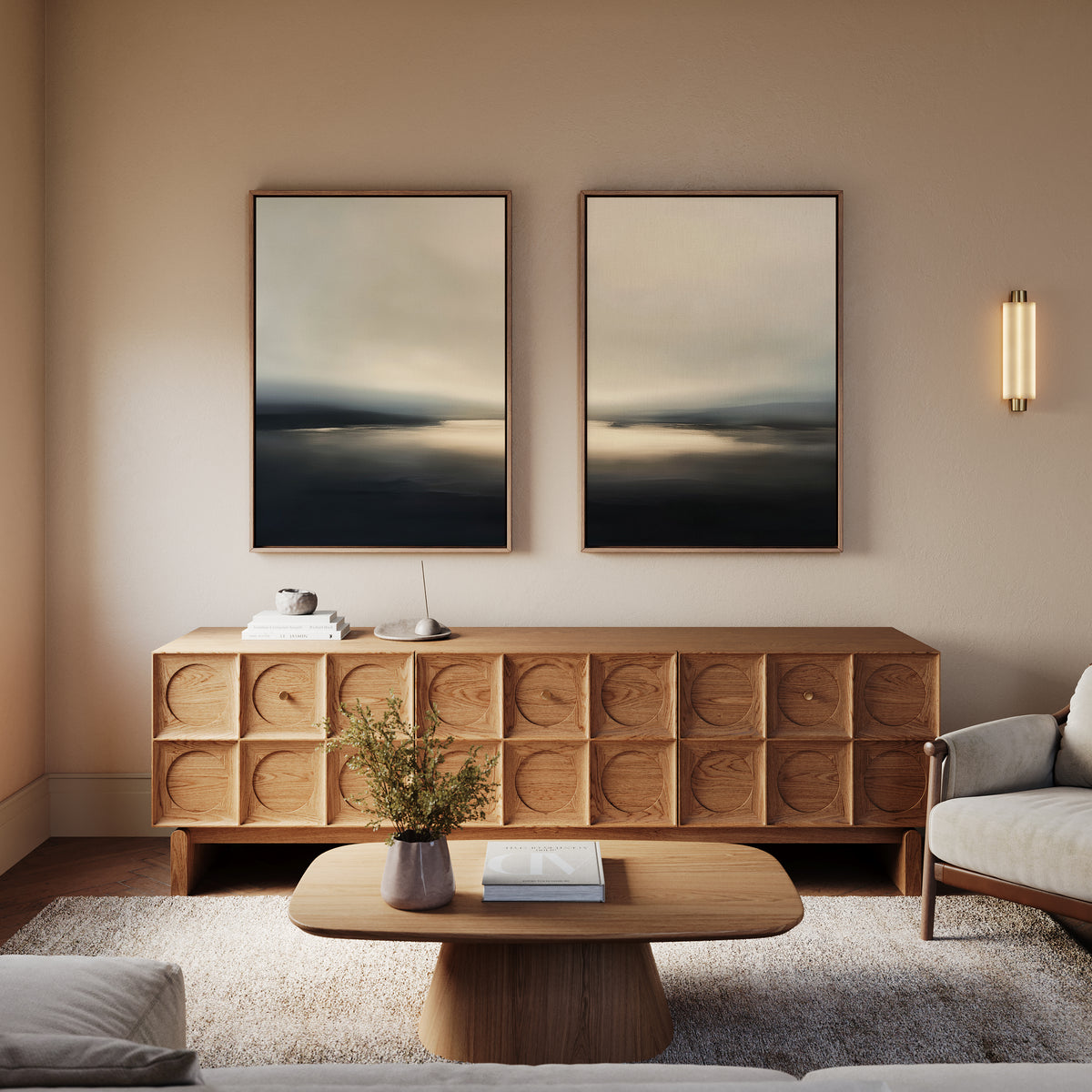 A modern living room with a wooden sideboard, coffee table, neutral armchair, Golden Fog Horizon - Set Of 2 wall art above, a sconce light, and a vase with flowers on the coffee table.